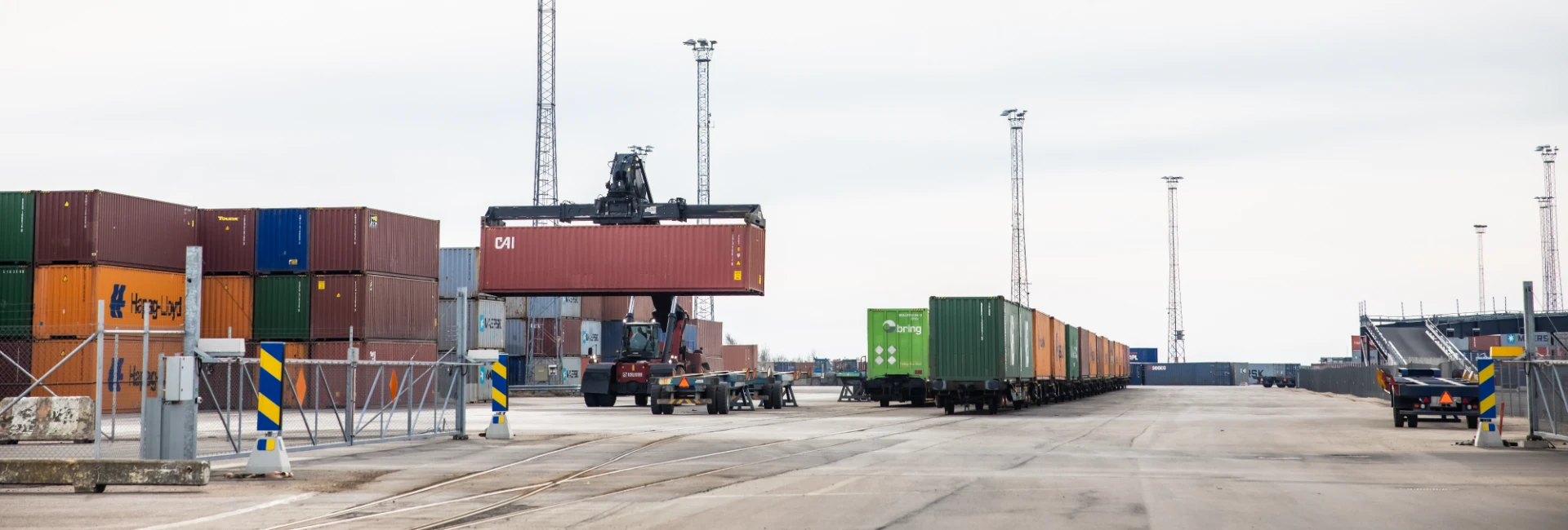 Truck kör container och tågvagnar står parkerade i hamnmiljö